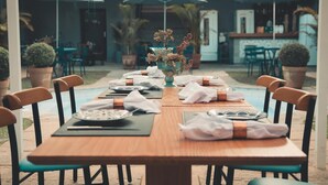 A dining area with a long wooden table set for a meal, surrounded by chairs, with umbrellas and potted plants in the background. - Casa Rosa Hotel Boutique (Petrópolis)