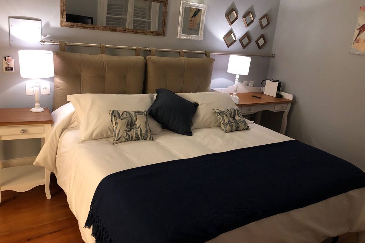 A neatly arranged bedroom with a bed, bedside tables, a desk, and a chair.