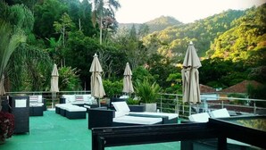 A rooftop lounge area with multiple lounge chairs and umbrellas, surrounded by lush greenery and hills. - Casa Rosa Hotel Boutique (Petrópolis)