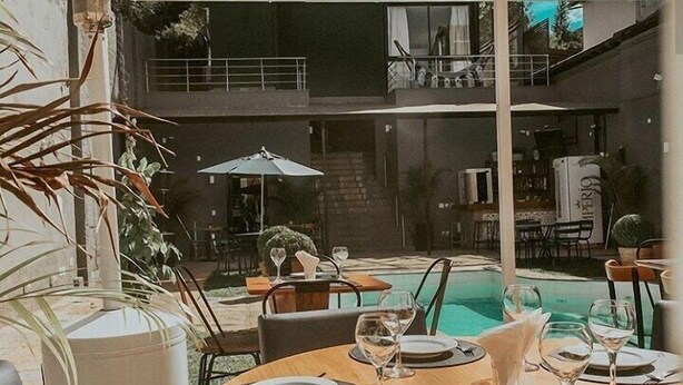 An outdoor dining area with round tables, chairs, and umbrellas. There is a pool in the background. - Casa Rosa Hotel Boutique (Petrópolis)
