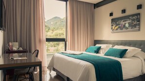 A hotel room with a bed, a desk, and a view of a mountain. - Casa Rosa Hotel Boutique (Petrópolis)