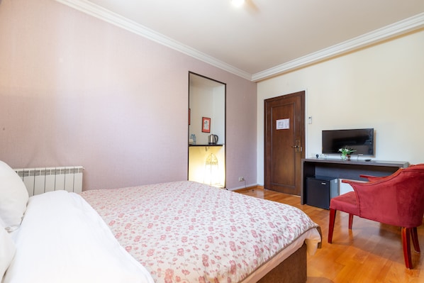 A bedroom with a bed, a desk with a TV, a red chair, and a small fridge.