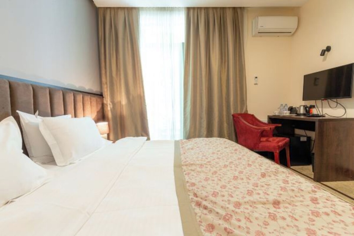 A hotel room with a bed, a desk, a chair, a television, and an air conditioning unit.
