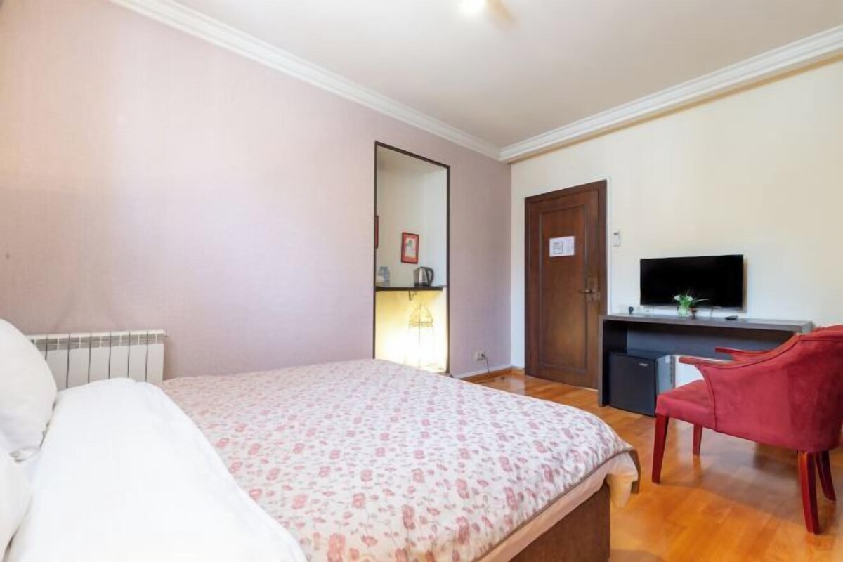 A bedroom with a bed, a desk with a television, and a red chair.