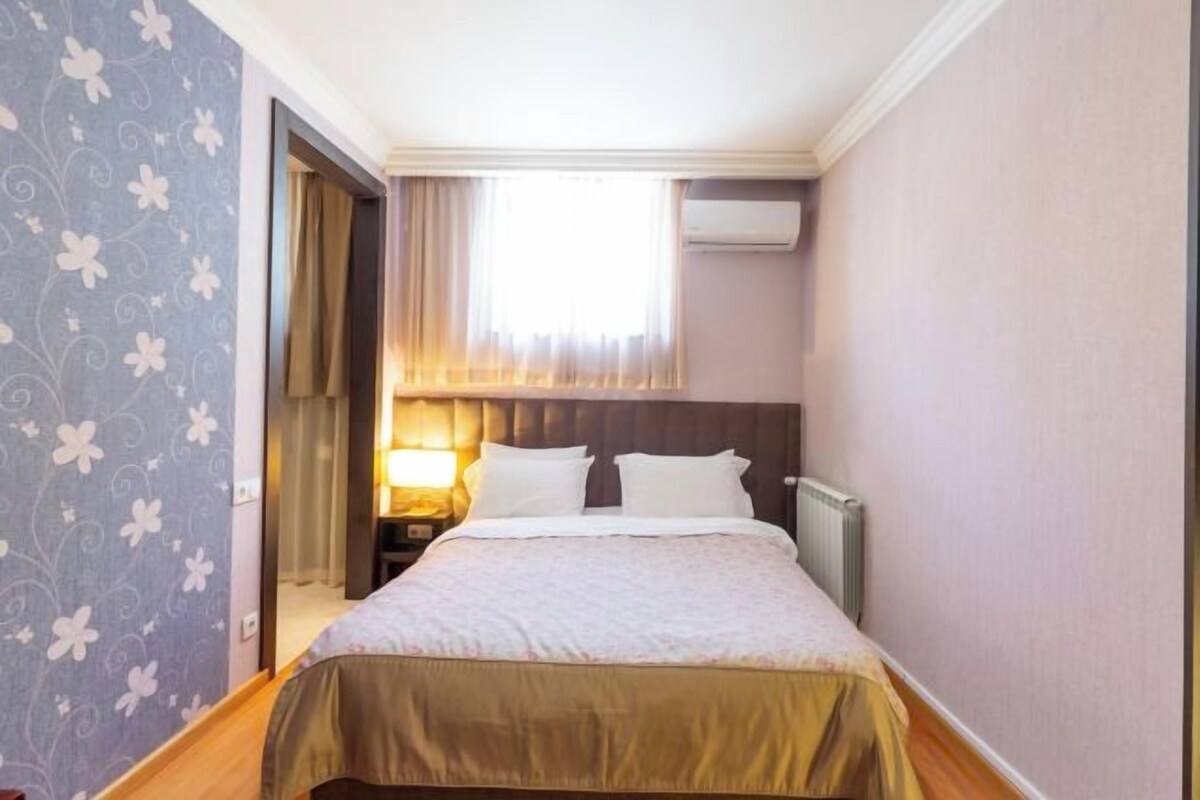 Een hotelkamer met een bed, nachtkastje, raam met gordijnen en een airconditioning.
