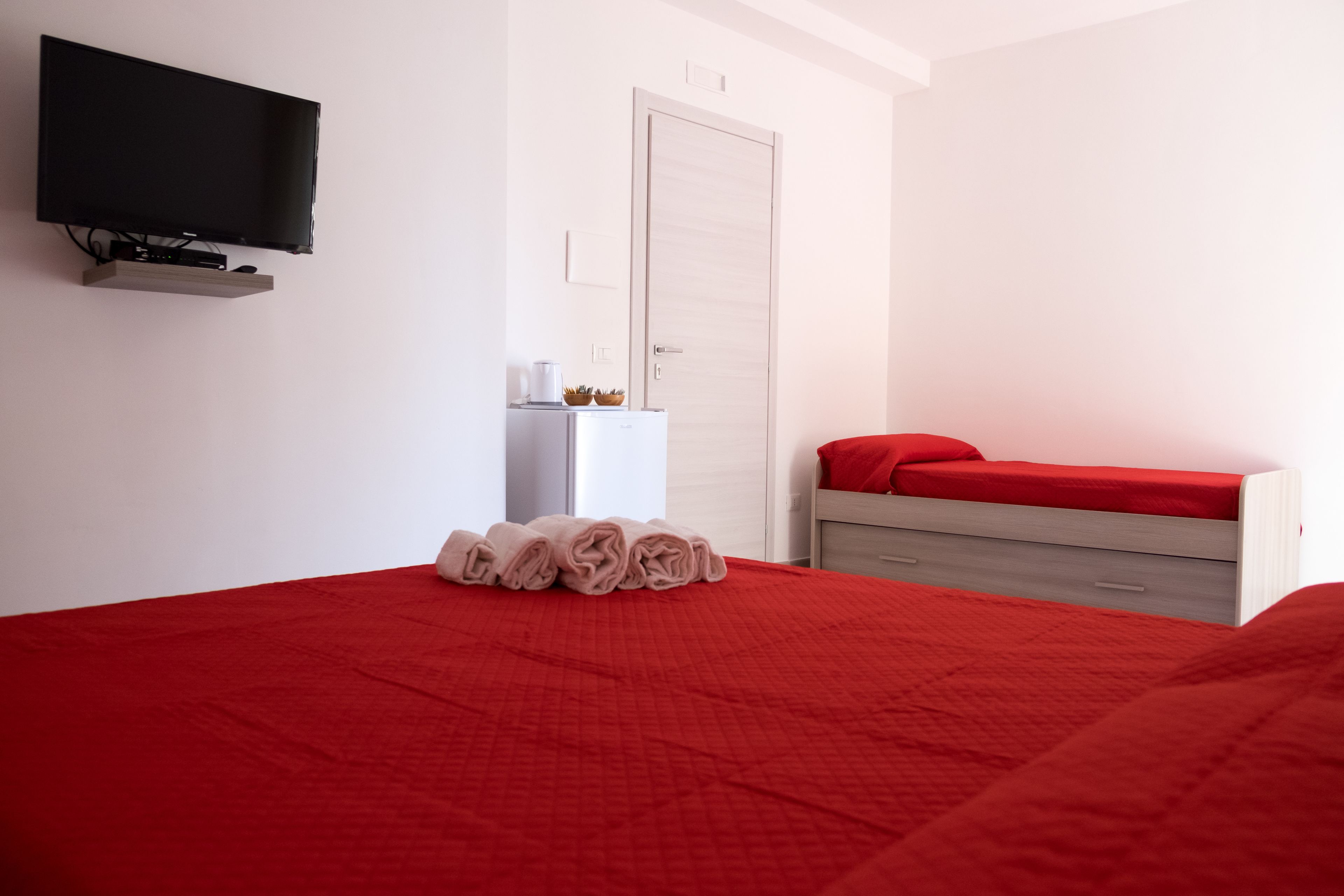 A hotel room with a large bed, a television mounted on the wall, a small table with a coffee maker, and a wardrobe.