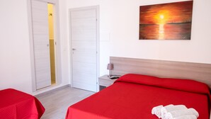Une chambre d’hôtel avec un lit, une table de chevet avec une lampe, un tableau représentant un coucher de soleil et une porte donnant sur une salle de bain.