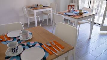 Un coin repas avec des chaises blanches et une table en bois, dressée pour deux personnes.