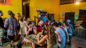 A crowded indoor space with people gathered around tables, some eating and others conversing. - Bella's Backpackers (San Ignacio)