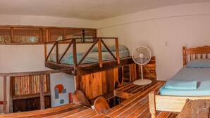 A rustic room with a loft bed, a wooden desk, and a standing fan. - Bella's Backpackers (San Ignacio)