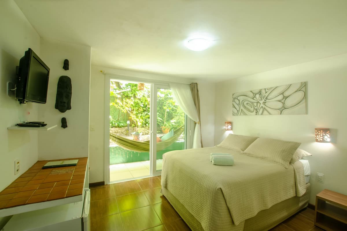 Une chambre avec un lit, une télévision et un hamac à l’extérieur de la porte-fenêtre coulissante, ainsi qu’une œuvre d’art accrochée au mur.
