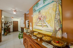 A buffet area with a variety of food items and a mural on the wall. - Pousada Borboleta (Cairu)