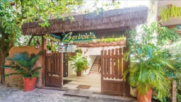 A rustic entrance with a thatched roof, a wooden gate, and potted plants. - Pousada Borboleta (Cairu)