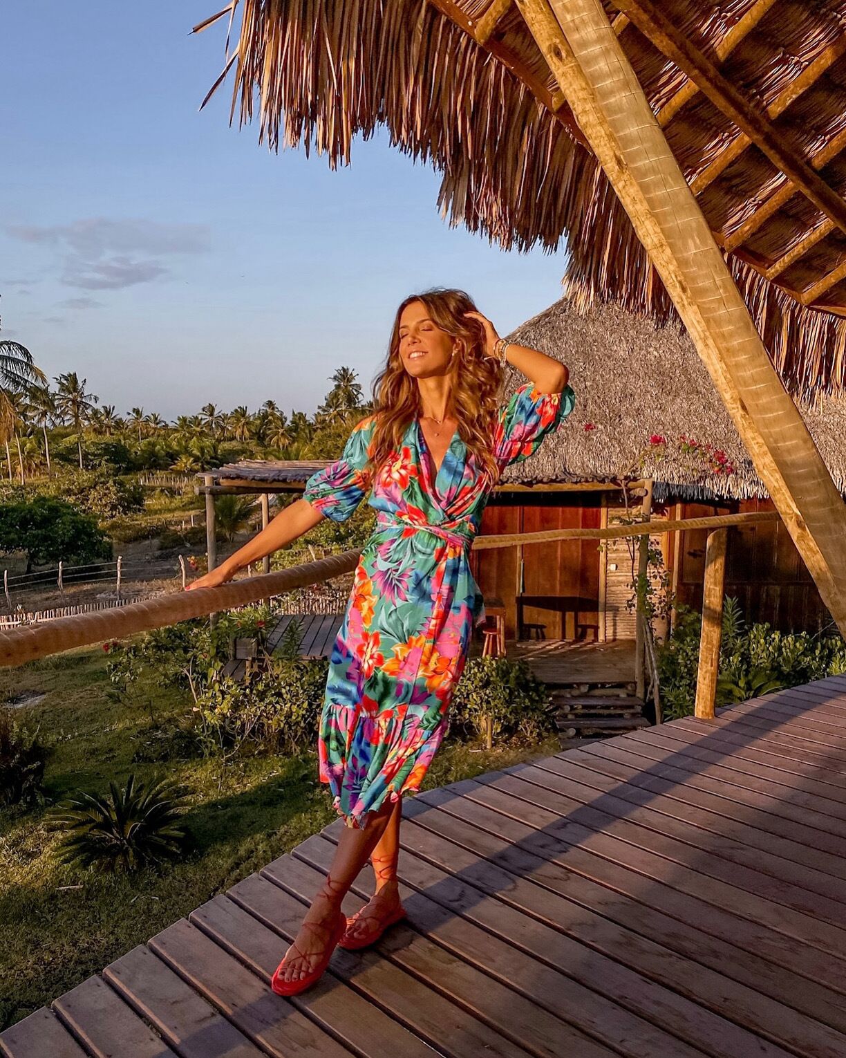 A person standing on a wooden deck with a thatched roof structure in the background.