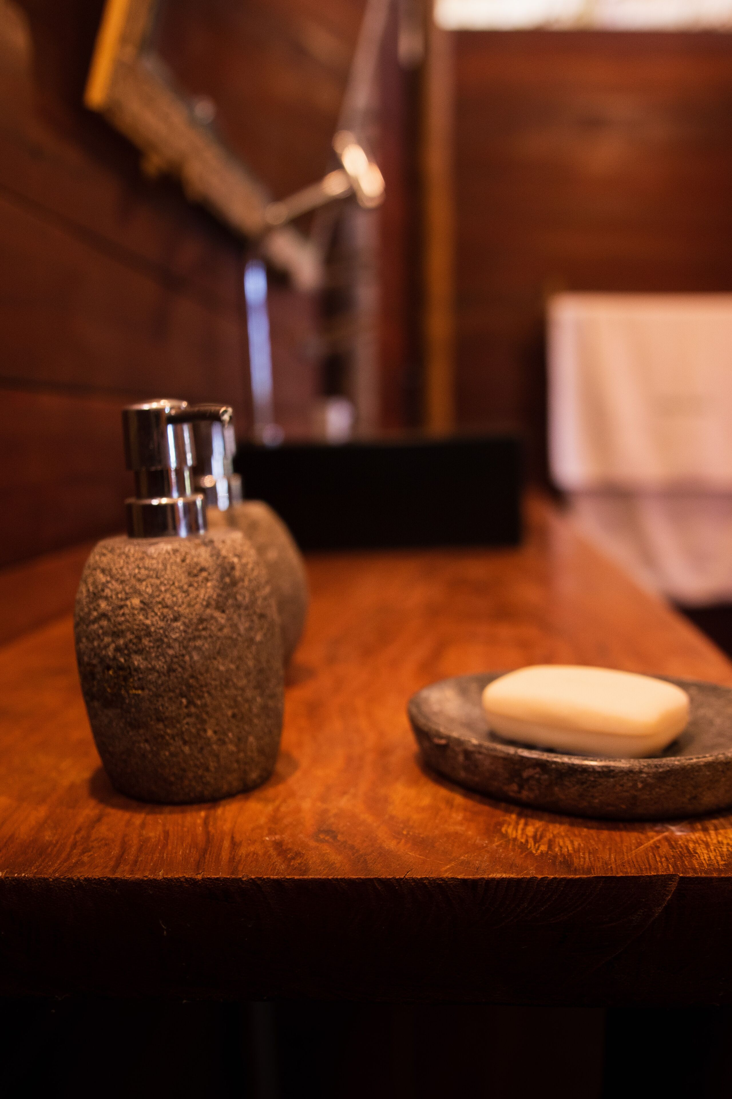 A wooden counter with two stone soap dispensers and a soap bar on a stone plate.