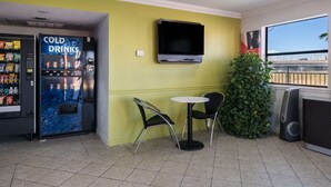 Un petit espace intérieur comprenant un distributeur automatique portant l’inscription « BOISSONS FRAÎCHES », un téléviseur fixé au mur et une petite table avec deux chaises.