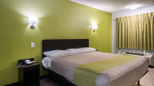 Une chambre d’hôtel avec un lit, une table de chevet avec un téléphone et un luminaire fixé au mur.