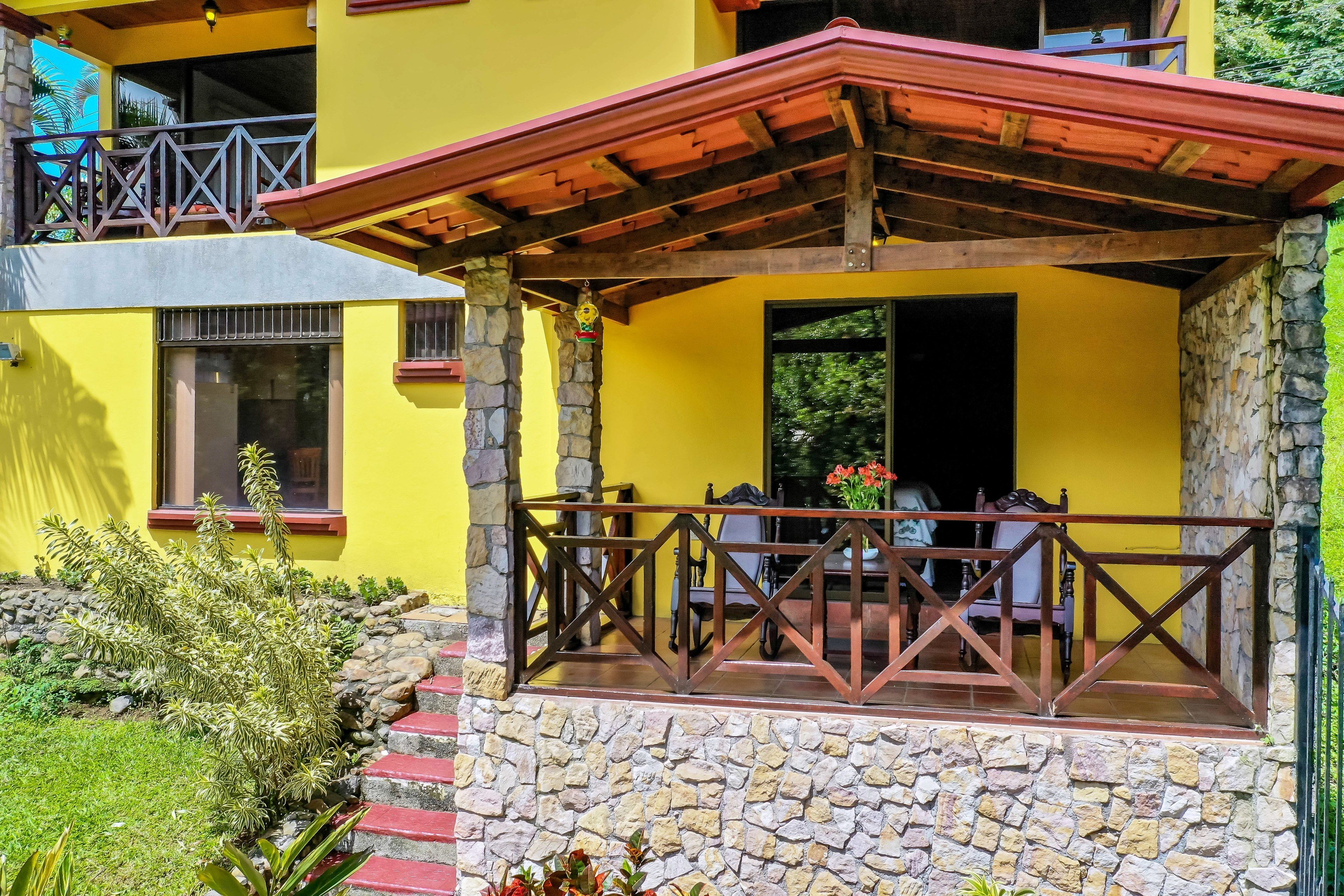 Un edificio amarillo con una escalera de piedra, un balcón de madera y un muro de piedra.