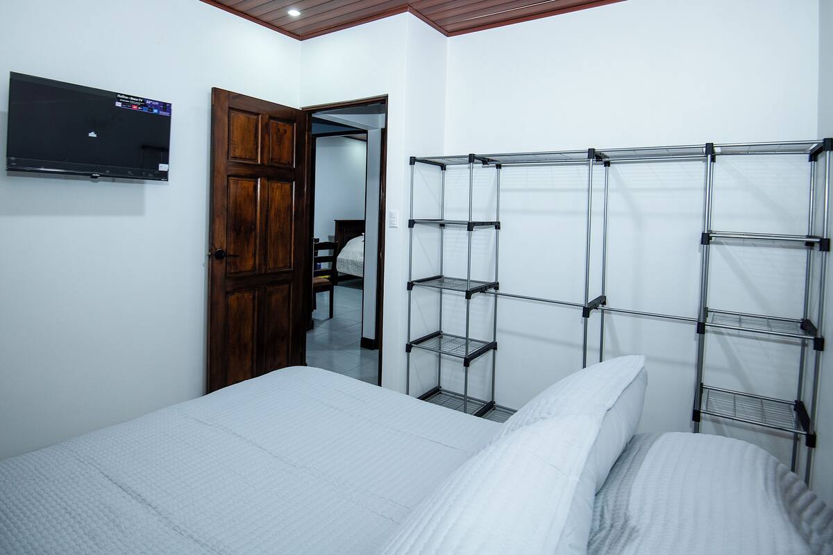 Een slaapkamer met een bed, een aan de muur bevestigde televisie en een houten kledingkast.