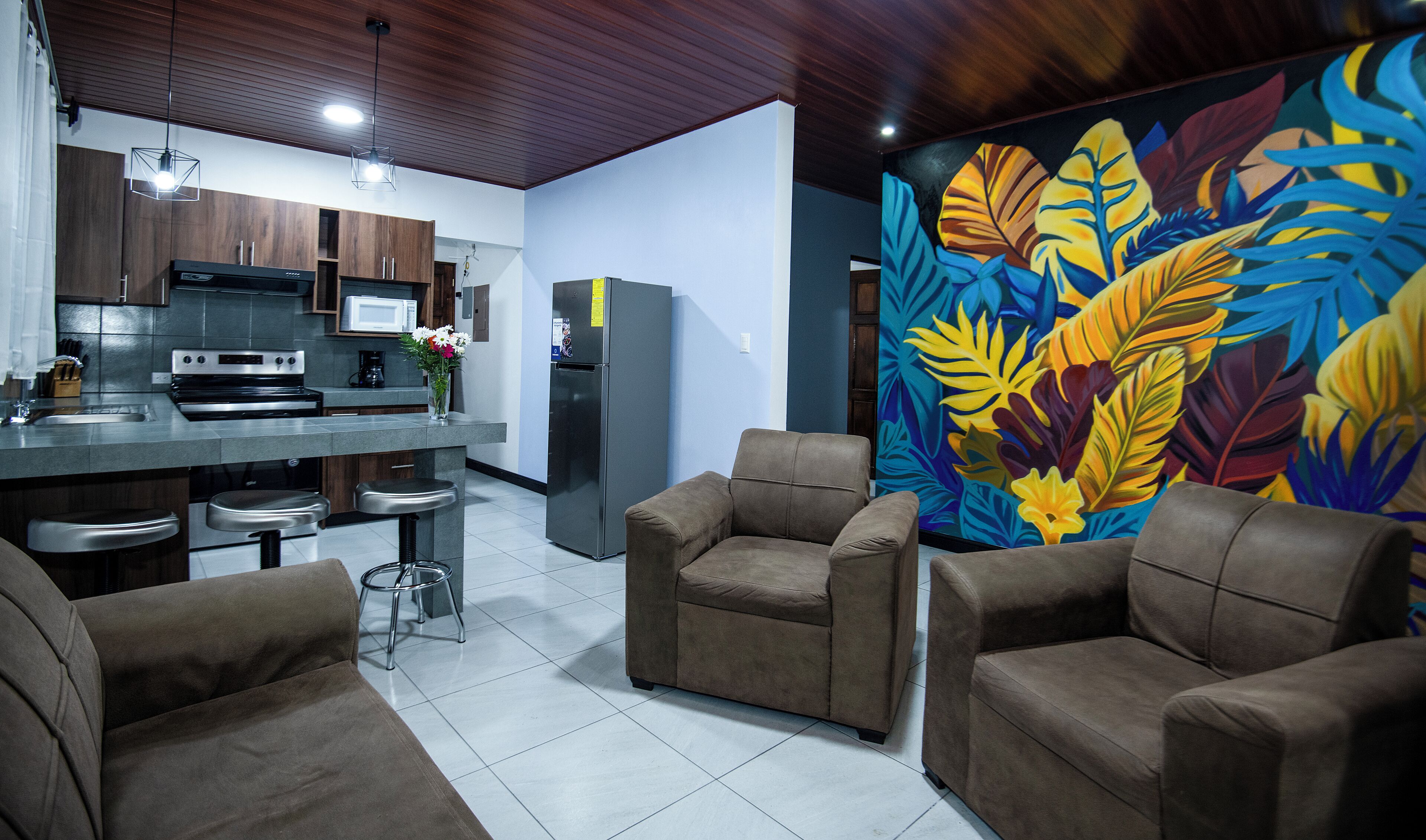 A modern kitchen with a dining area, featuring a large island, bar stools, and a vibrant leaf-patterned wall.