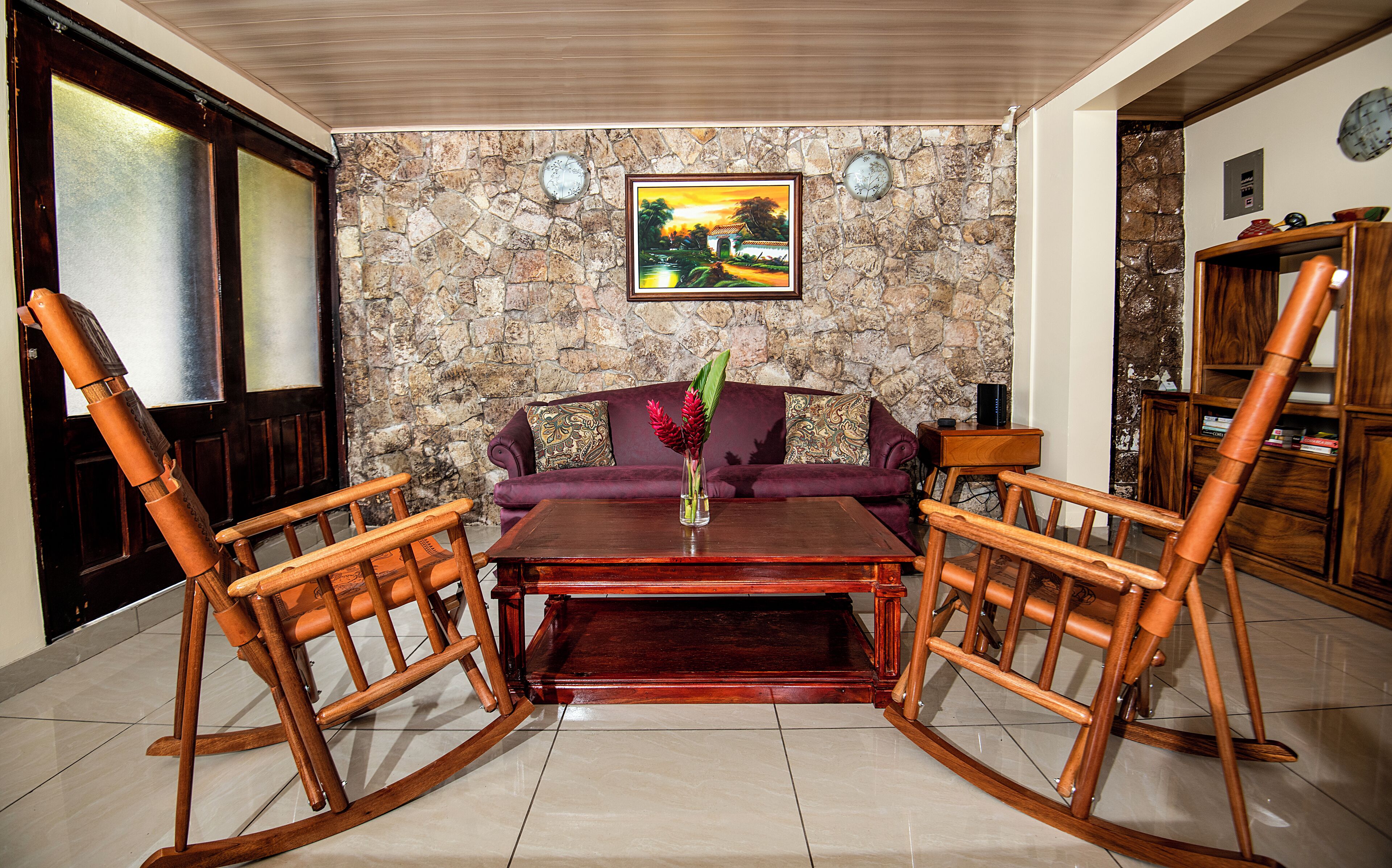 A living room with a stone wall, a sofa, a coffee table, and a wooden rocking chair.
