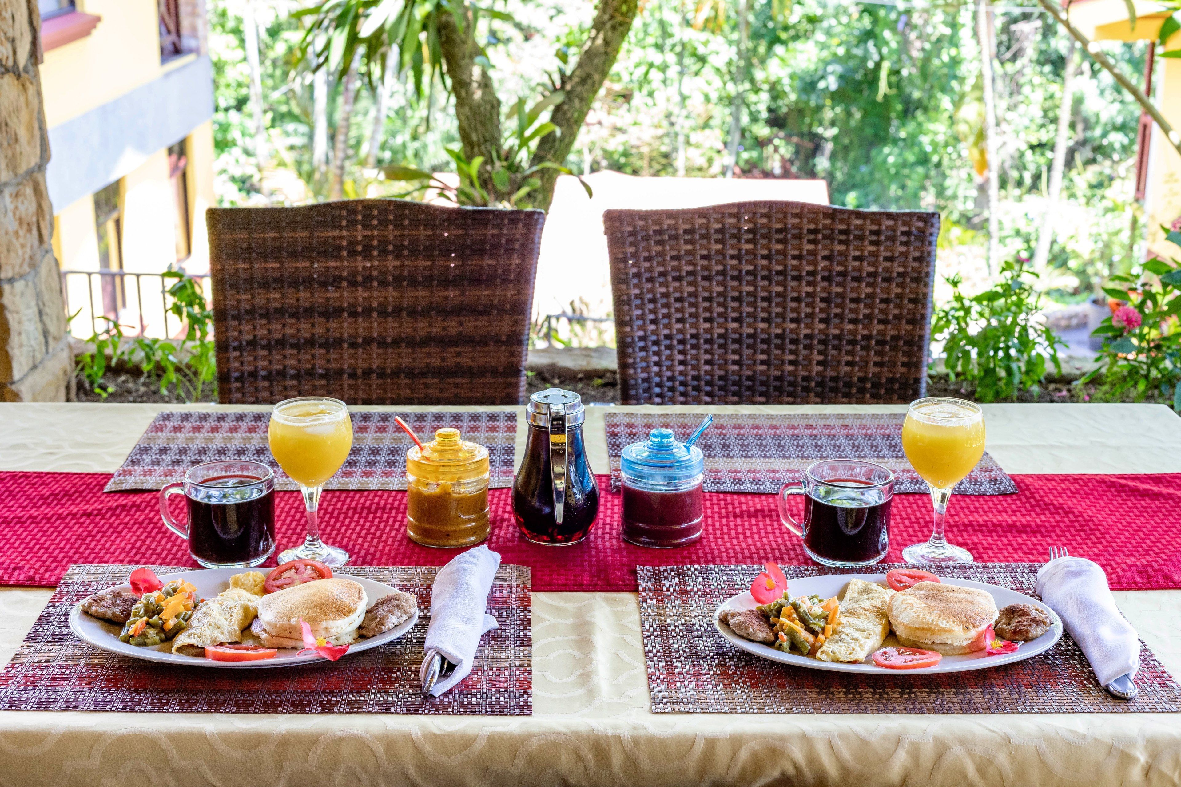 A breakfast setup with two plates of food, a coffee mug, and a juice glass on a table outdoors.