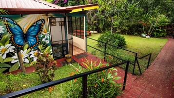 Un jardín con un mural de mariposa y flores, un banco rojo y un sendero que lleva a un edificio con techo de metal.
