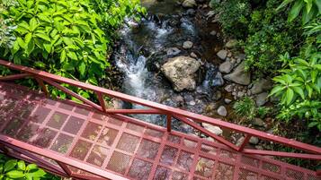 A red metal bridge over a stream with rocks and greenery on either side.