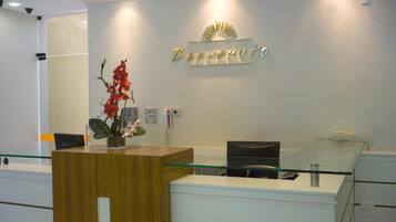 A reception desk with a wooden counter and a glass top, a vase with red flowers, and a wall sign that reads "Benvenuto".