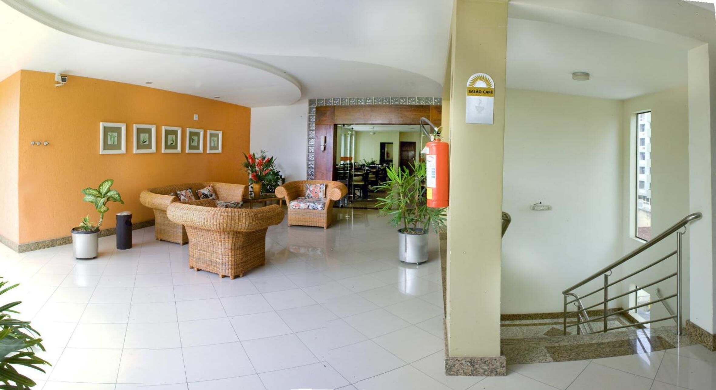 A spacious lobby with wicker furniture, potted plants, and a staircase.