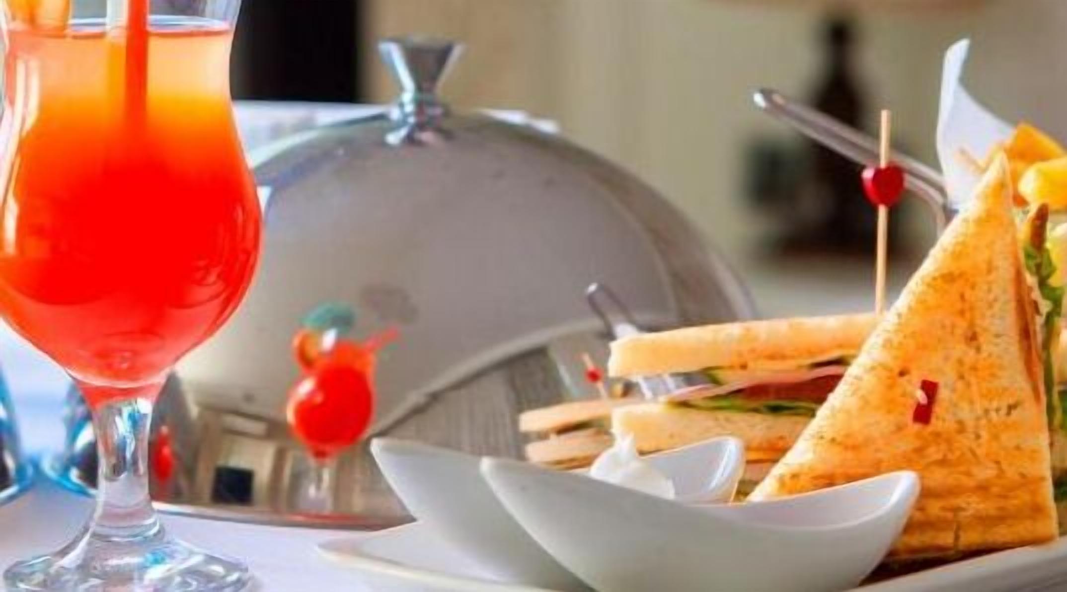 A tray with a sandwich and a glass of red drink, possibly a cocktail, on a table.