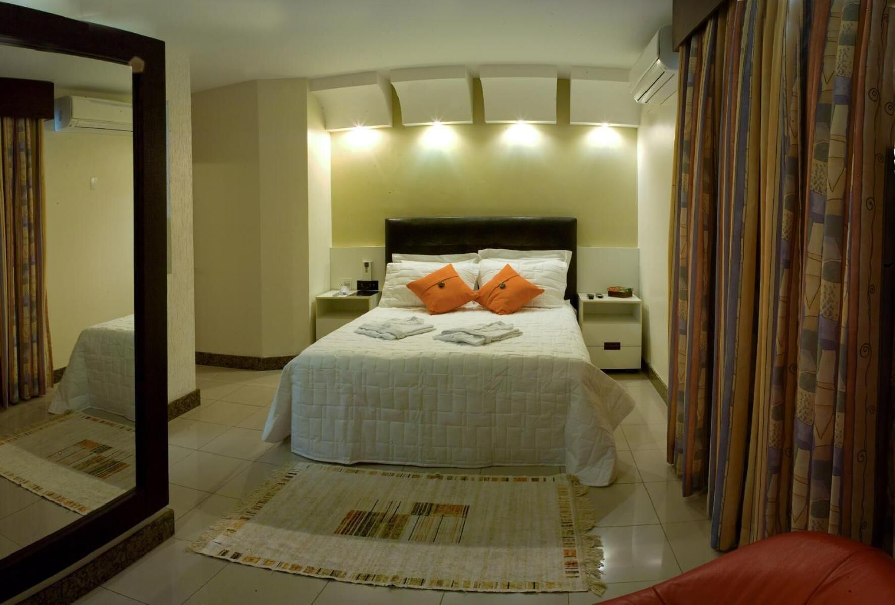 Una habitación de hotel con una cama grande, dos mesitas de noche, un espejo y una alfombra estampada.