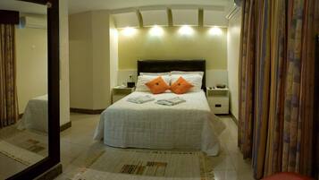 Una habitación de hotel con una cama grande, dos mesitas de noche, un espejo y una alfombra estampada.