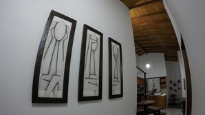A hallway with three framed abstract paintings on the wall, leading to a kitchen area with wooden cabinets and a dining table. - Fami Hotel Vive Jardin - Hostel (Jardin)