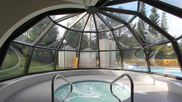 A glass-enclosed hot tub with a view of a swimming pool and trees. - Marquise Condos by Whistler Retreats (Whistler)
