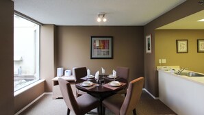 A dining area with a round table set for four, equipped with plates, glasses, and cutlery. There are four chairs around the table, and a window provides natural light. - Marquise Condos by Whistler Retreats (Whistler)