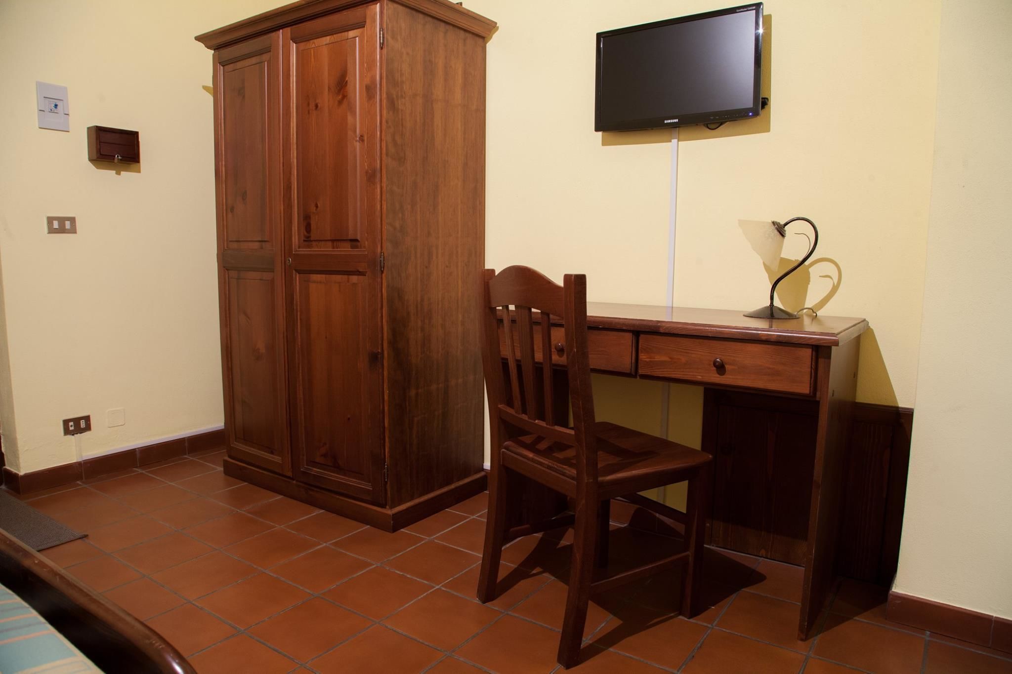 A room with a wooden desk, a chair, a television mounted on the wall, and a cabinet.
