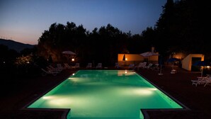 Une piscine au crépuscule, entourée de chaises longues et de parasols.