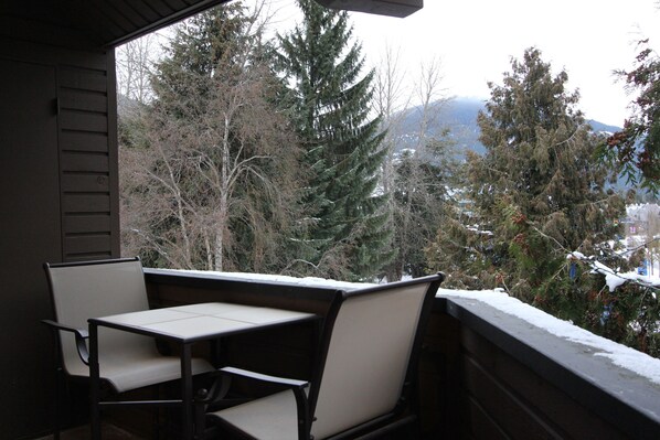 Un balcón con mesa y sillas, con vistas a un paisaje nevado con árboles y montañas.