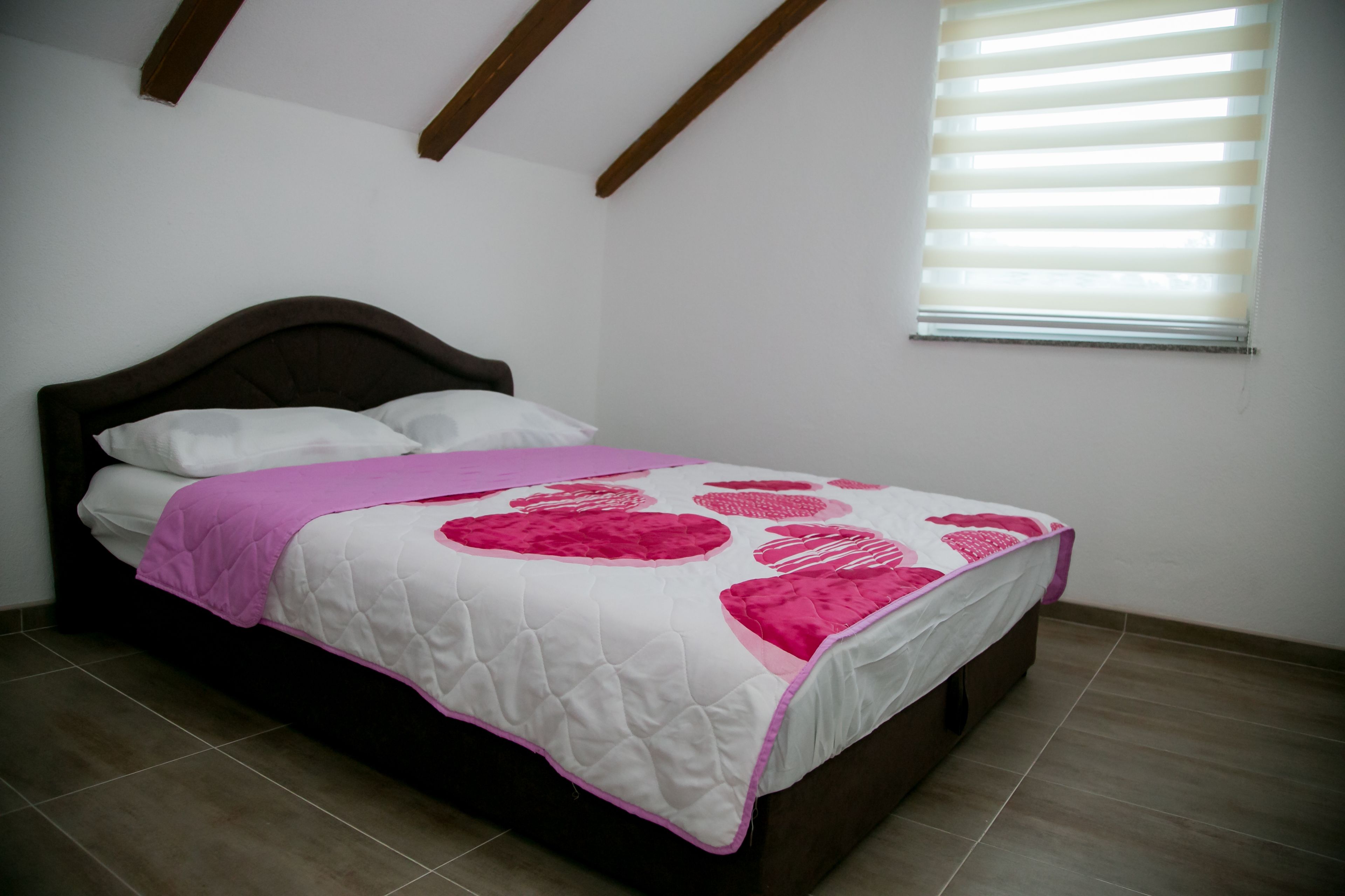 A bedroom with a bed, a window with blinds, and a sloped ceiling.