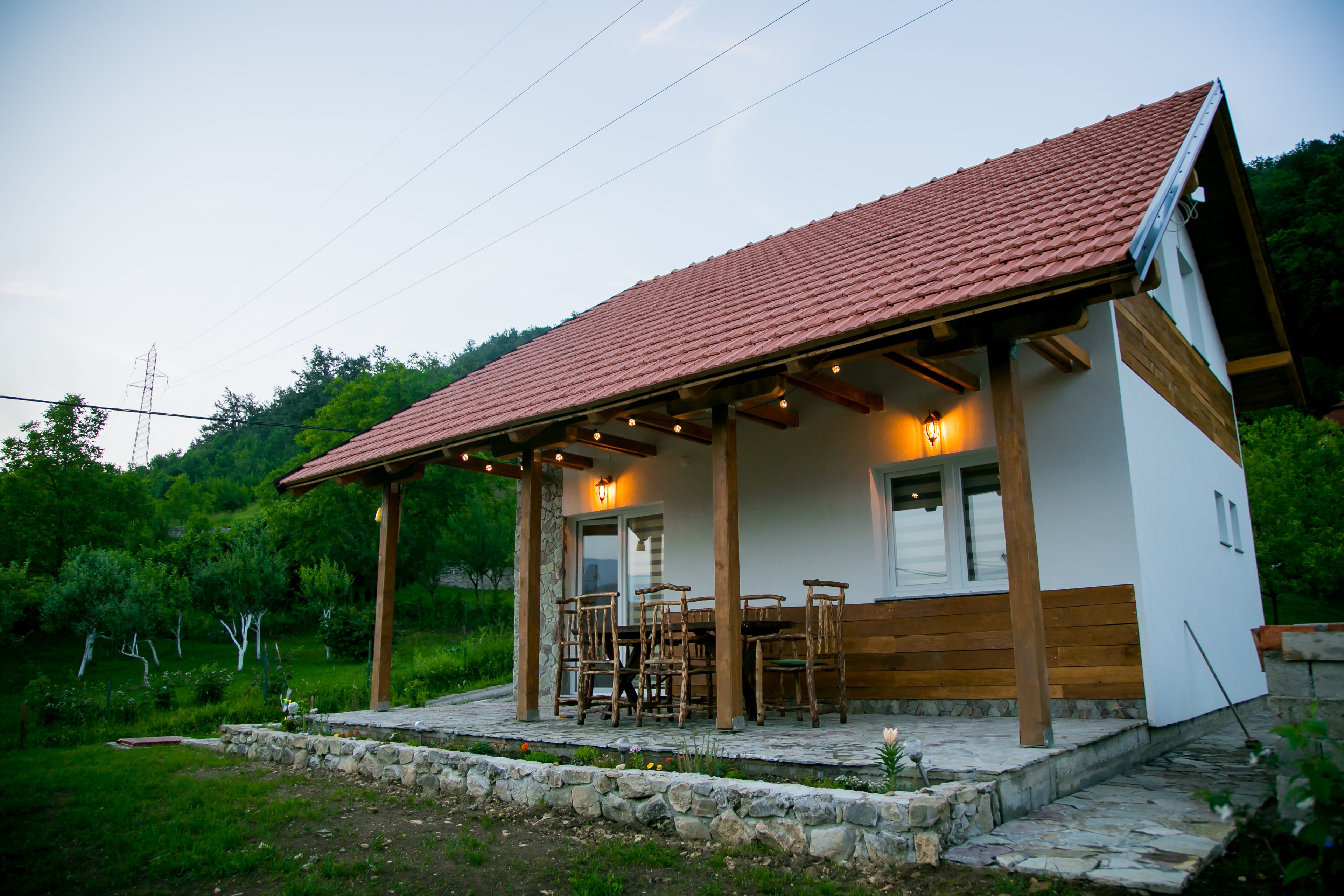 Ein kleines, eingeschossiges Haus mit Ziegeldach, einer überdachten Terrasse mit Holzmöbeln und einem Steinfundament.