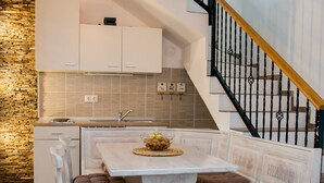 Una cocina con pared de piedra, armarios blancos y una escalera de madera.