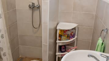 A bathroom with a shower, a sink, and a small window.