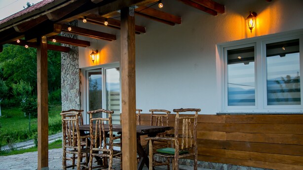 Una pérgola de madera al aire libre con un muro de piedra y una mesa con sillas.