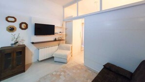 Ett vardagsrum med en platt-TV, en vit fåtölj, en brun soffa och ett träskåp.