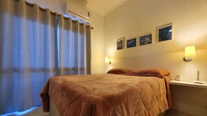 Ett hotellrum med en stor säng, ett nattduksbord med en lampa och ett fönster med gardiner.