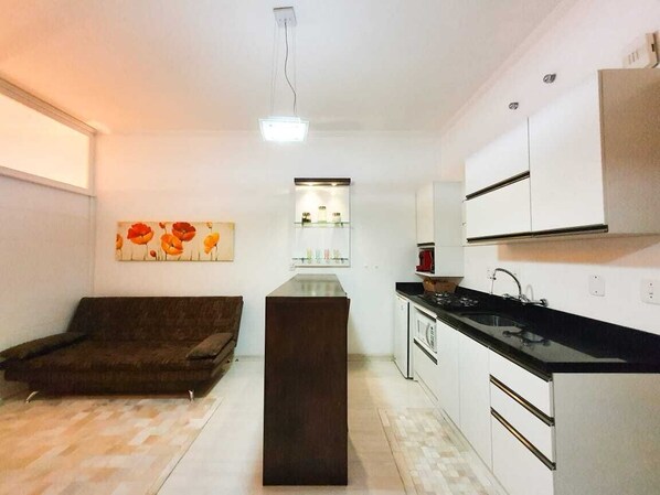 A modern kitchen with white cabinets, a black countertop, and a central island. There is a sofa and a painting on the wall.