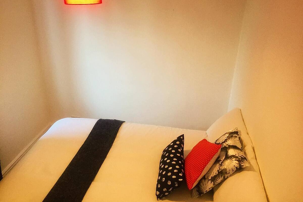 Hotellihuone, jossa on sänky, tyynyt ja seinään kiinnitetty valaisin.
