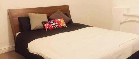 Ein Bett mit Holzvorhang, schwarz-weißer Bettwäsche und bunten Kissen.