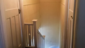 Un estrecho pasillo con puertas blancas y una escalera de madera.